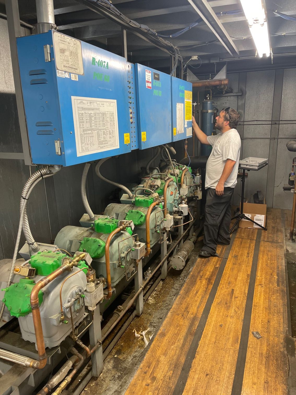 Technician inspecting green machinery beneath blue control panels in an industrial room
