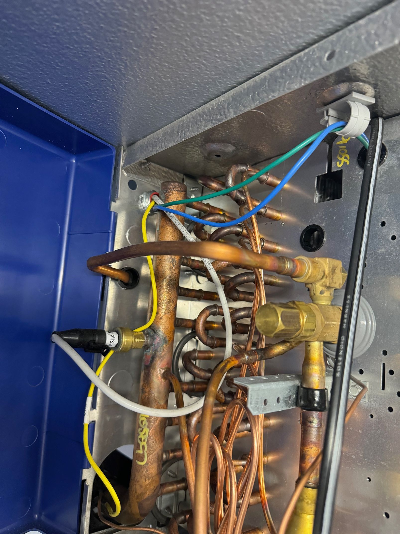 Close-up of exposed copper pipes and wiring inside a blue metal appliance panel.