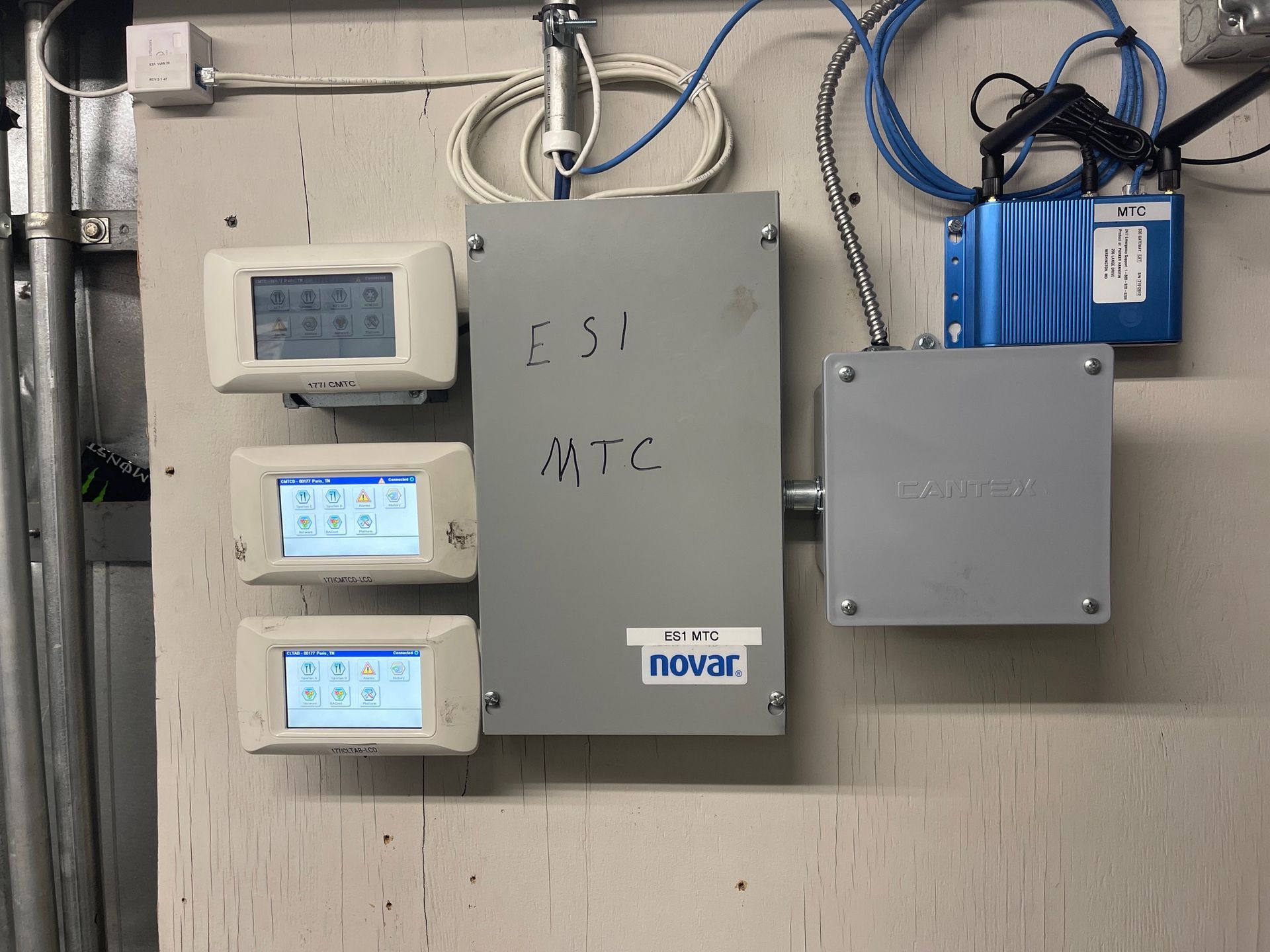 Electrical control panels and meters mounted on a wall with cables and blue equipment boxes