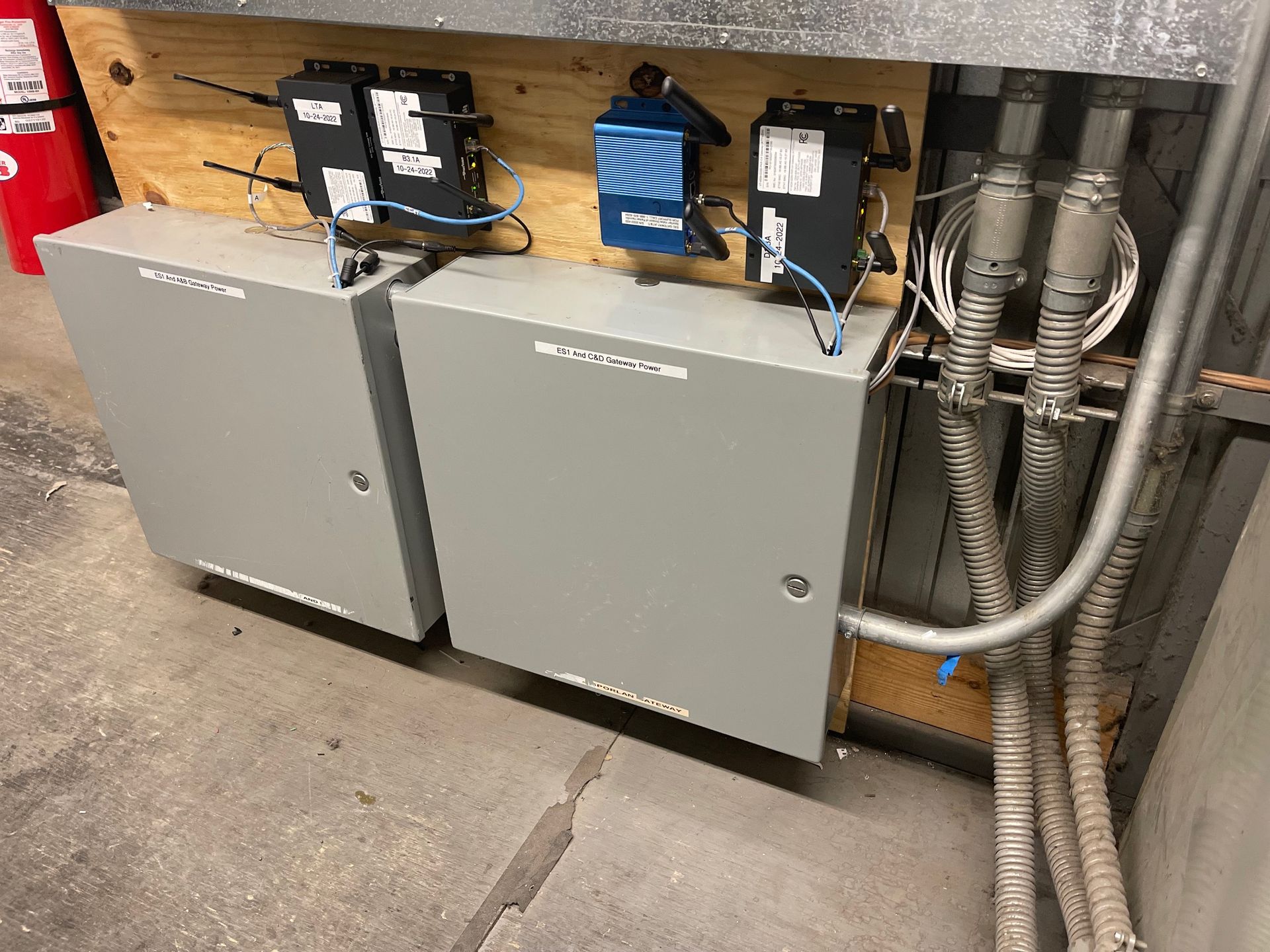 Two gray control cabinets mounted under piping and electrical equipment in a utility room.
