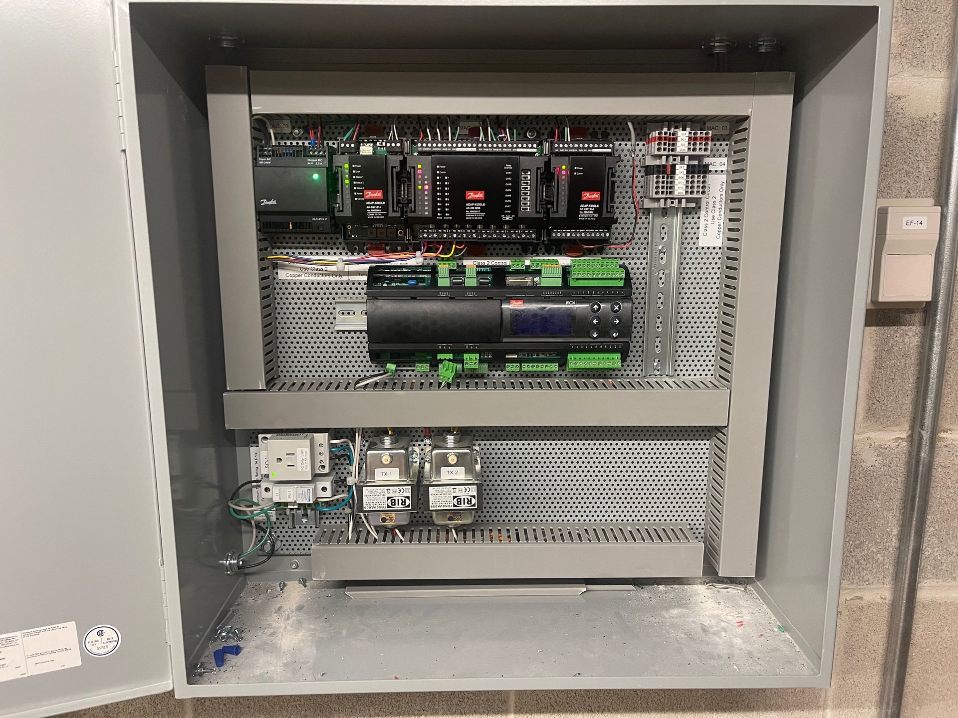 Open electrical control panel with circuit boards, wires, and mounted components inside a gray cabinet.