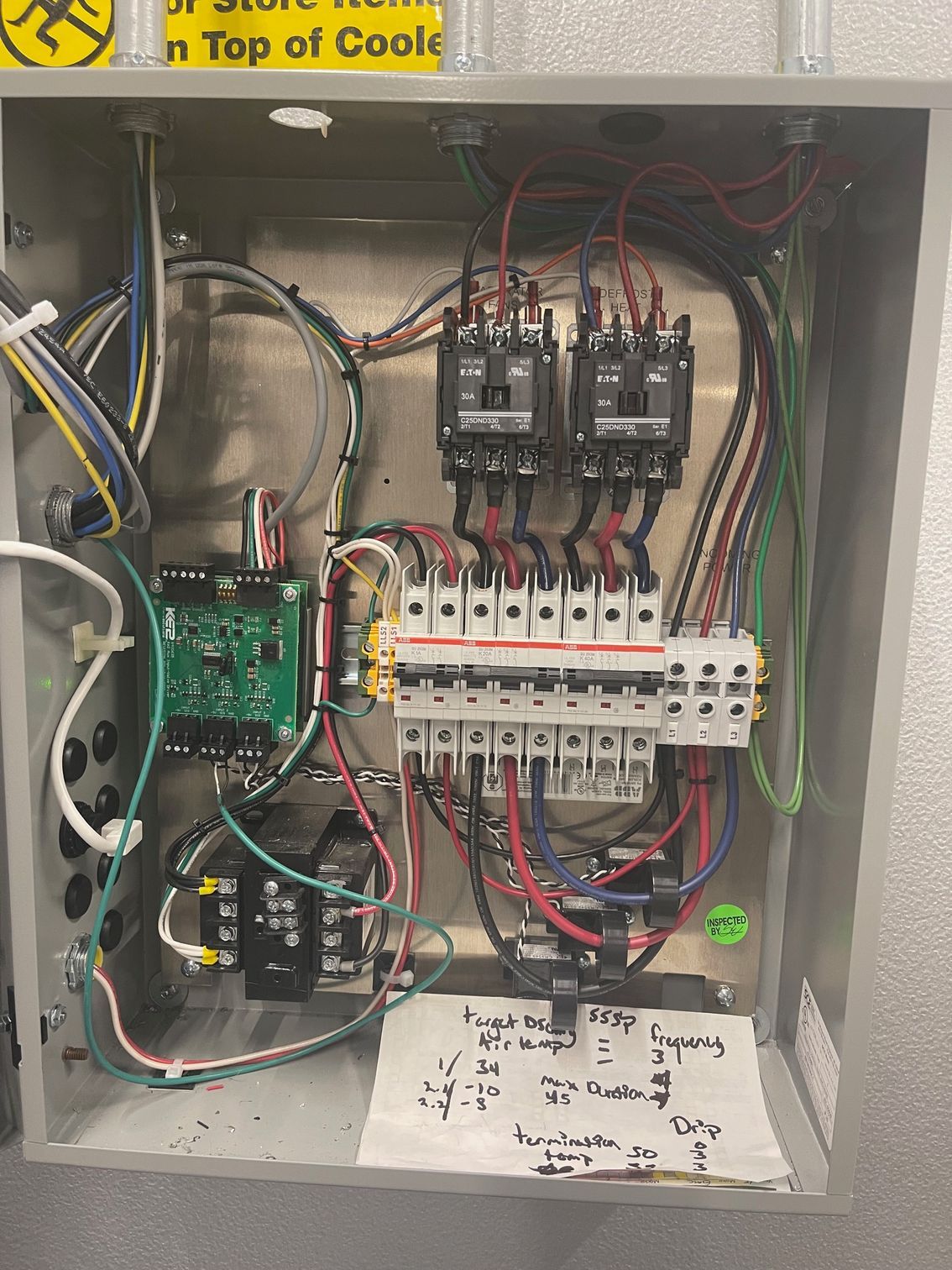 Open electrical control panel with relays, wiring, breakers, and handwritten notes on the bottom.