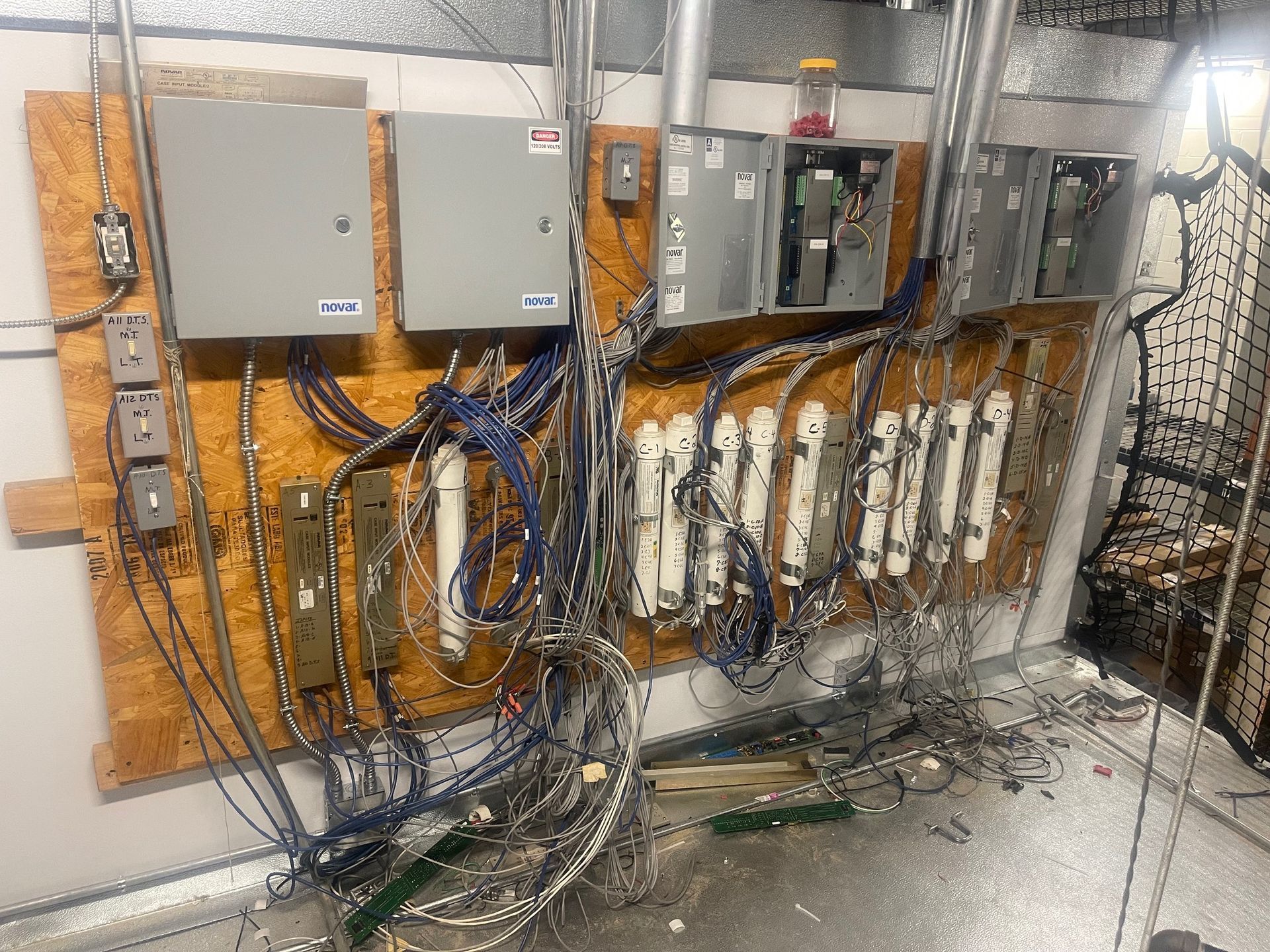 Electrical control panels and tangled wiring on a utility wall in a workshop.