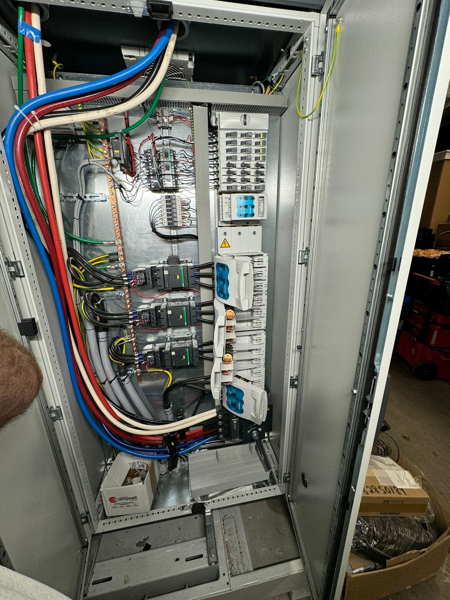 Open electrical control cabinet with wires, breakers, and circuit boards inside a metal enclosure.