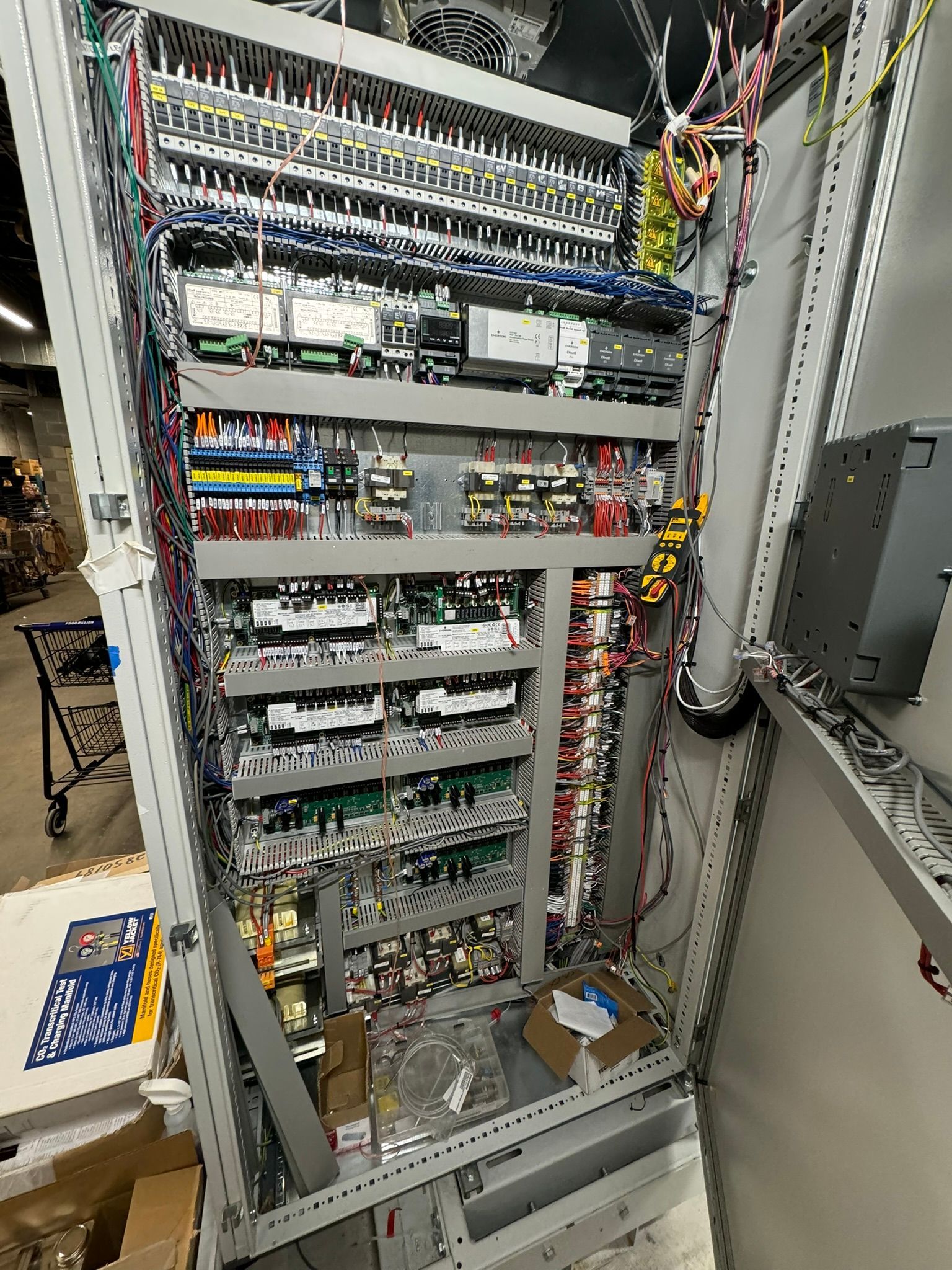 Open electrical control cabinet with wires, circuit boards, and terminal blocks inside a server-room setting
