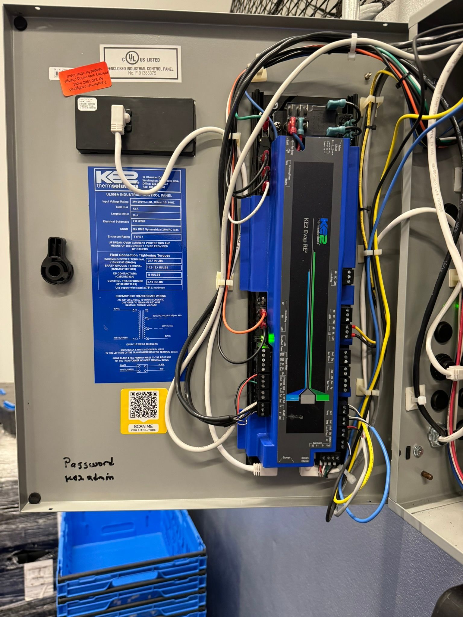 Open electrical cabinet with blue wiring panel, control module, and bundled cables inside a gray enclosure