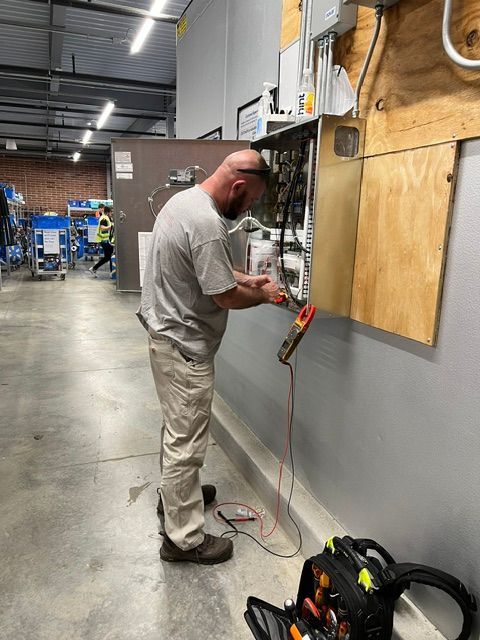 Man working on electrical wiring beside a gray wall in an industrial workshop
