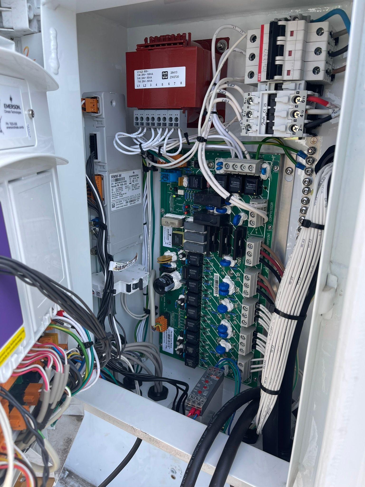 Open electrical control cabinet with circuit boards, wiring, and a red module inside.