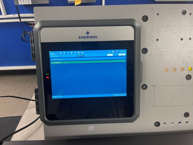 Gray industrial touchscreen panel with blue display mounted on a machine in a workshop