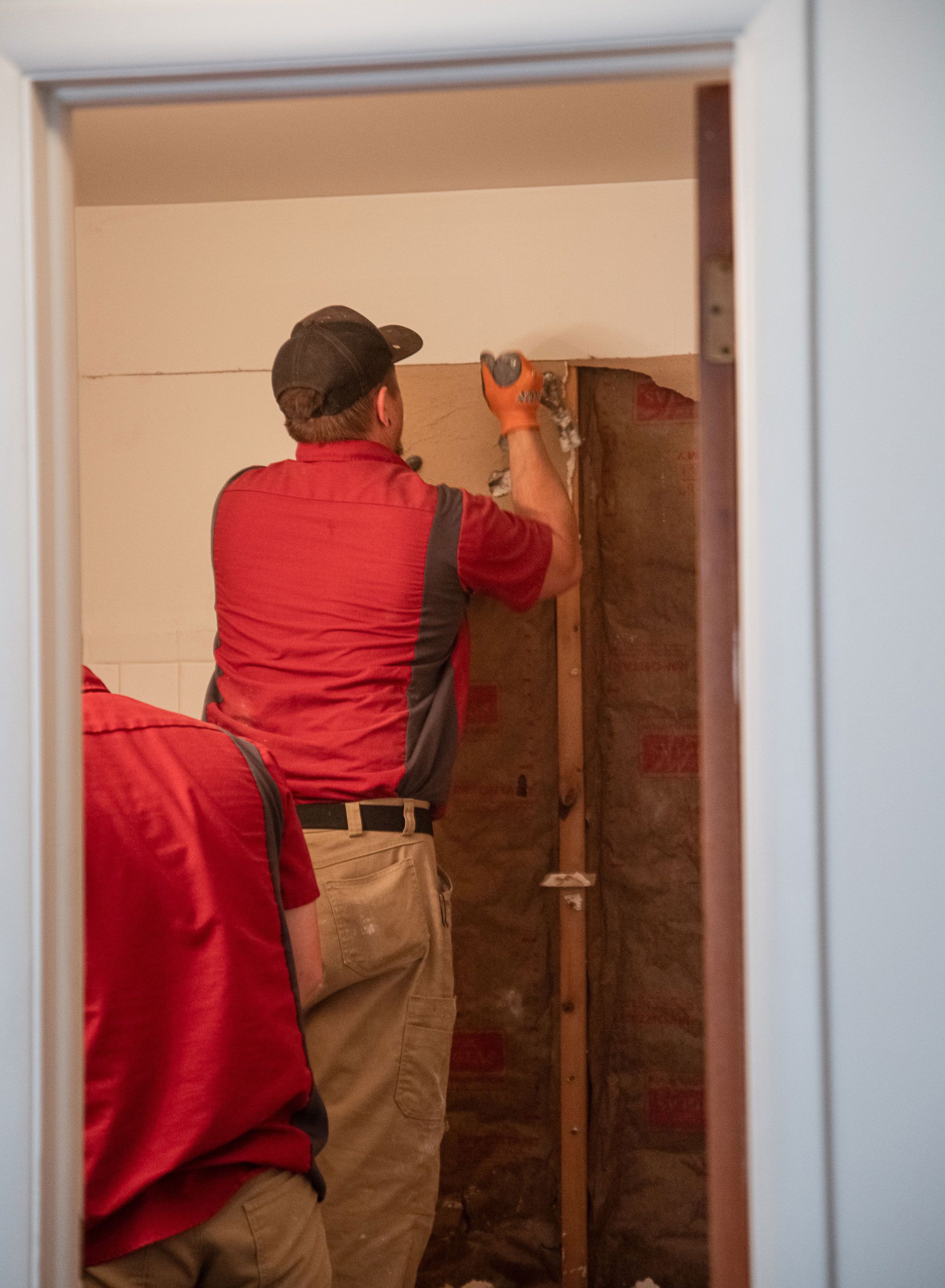 A man in a red shirt is working on a wall in a room