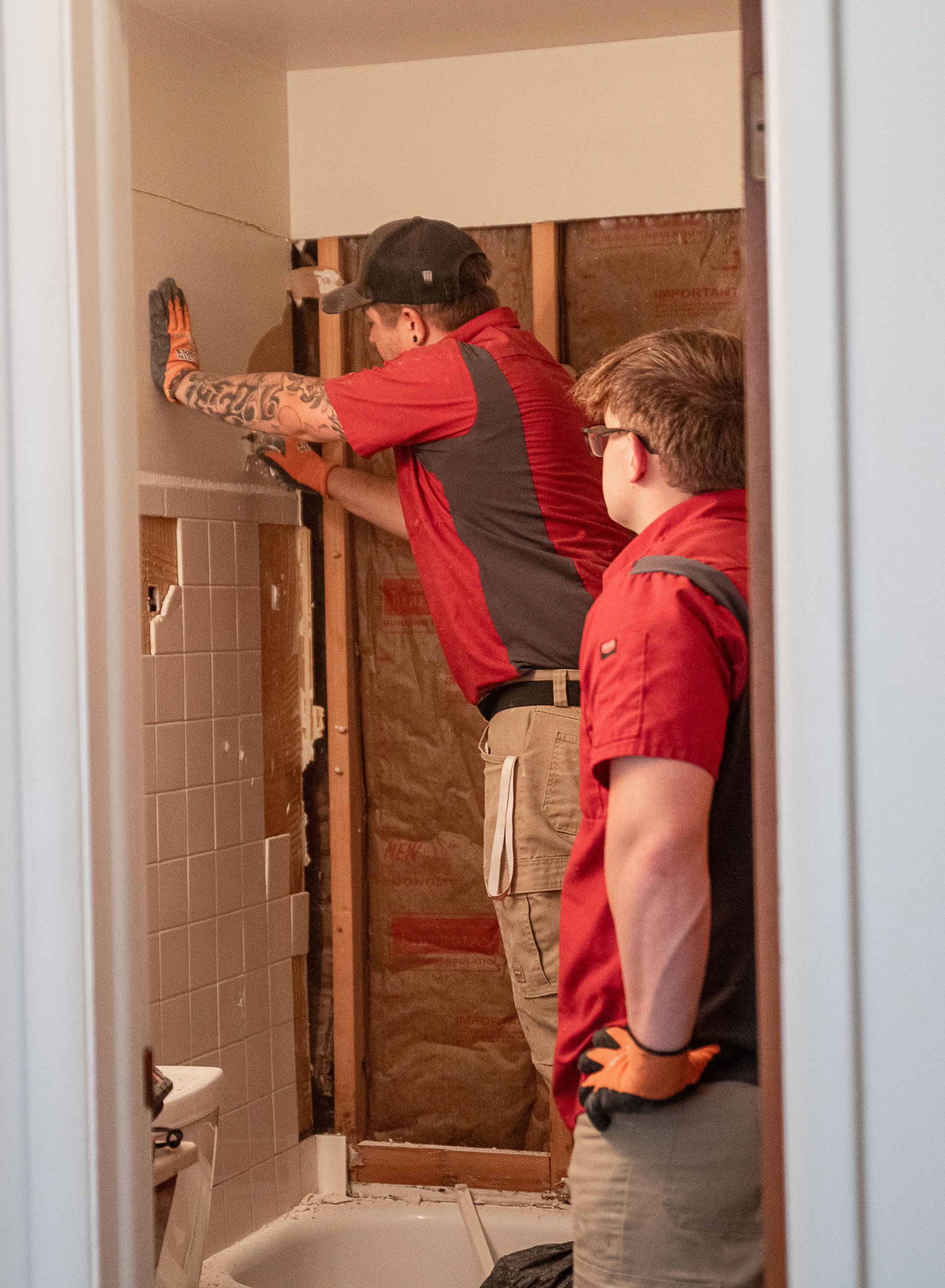 Two men are working on a bathroom wall