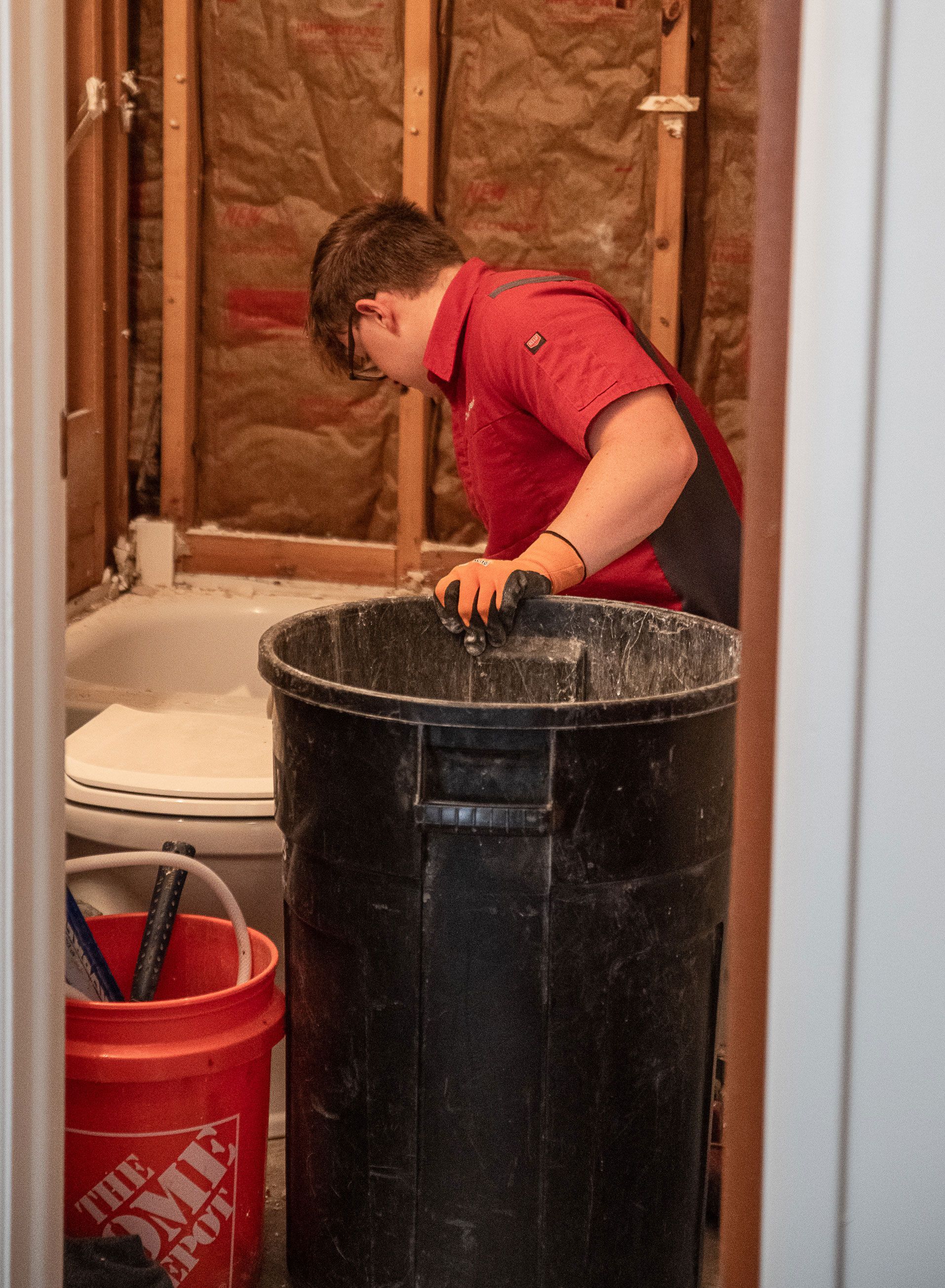 A man is standing next to a trash can in a bathroom