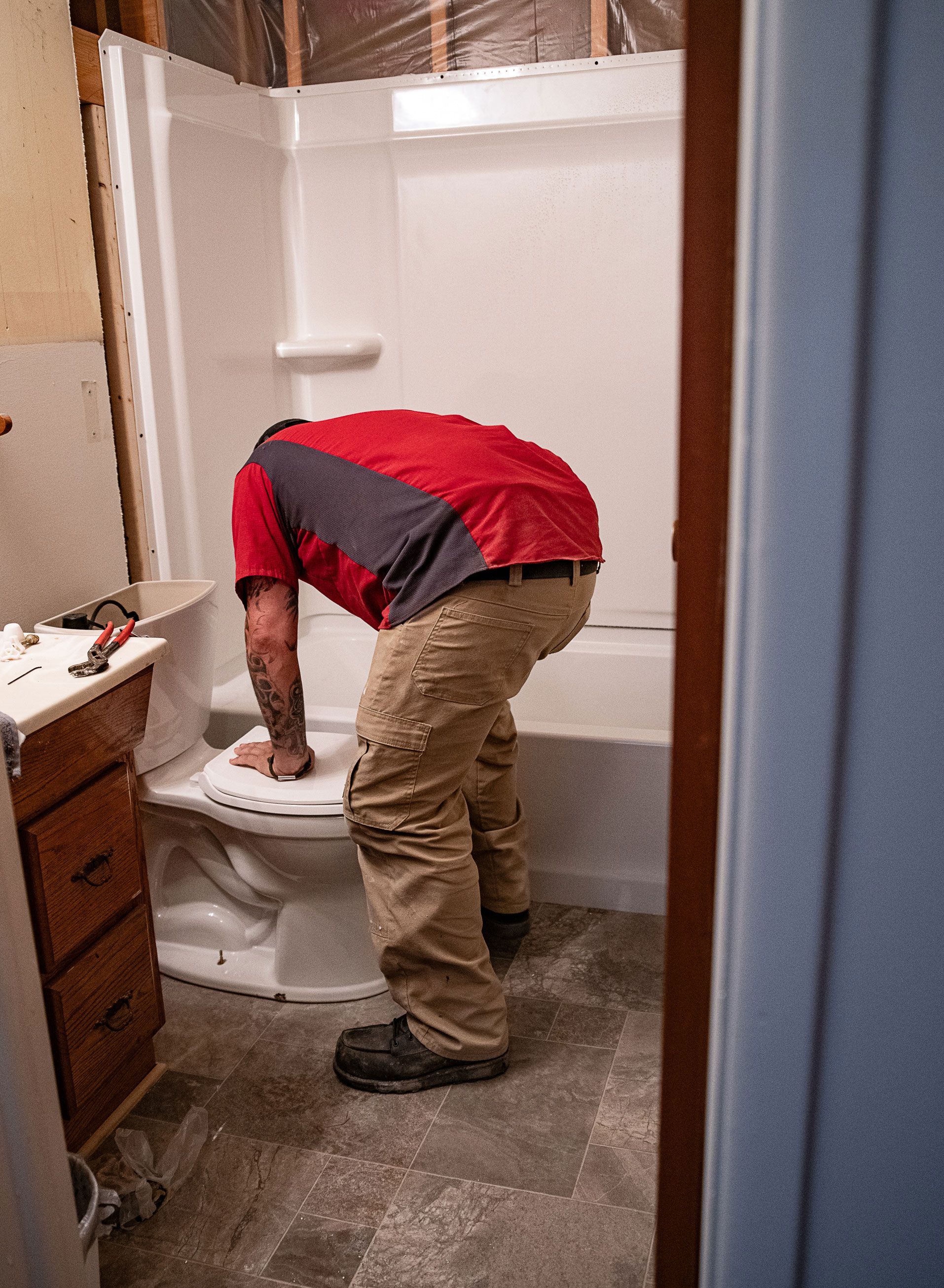 A man is bending over to fix a toilet in a bathroom