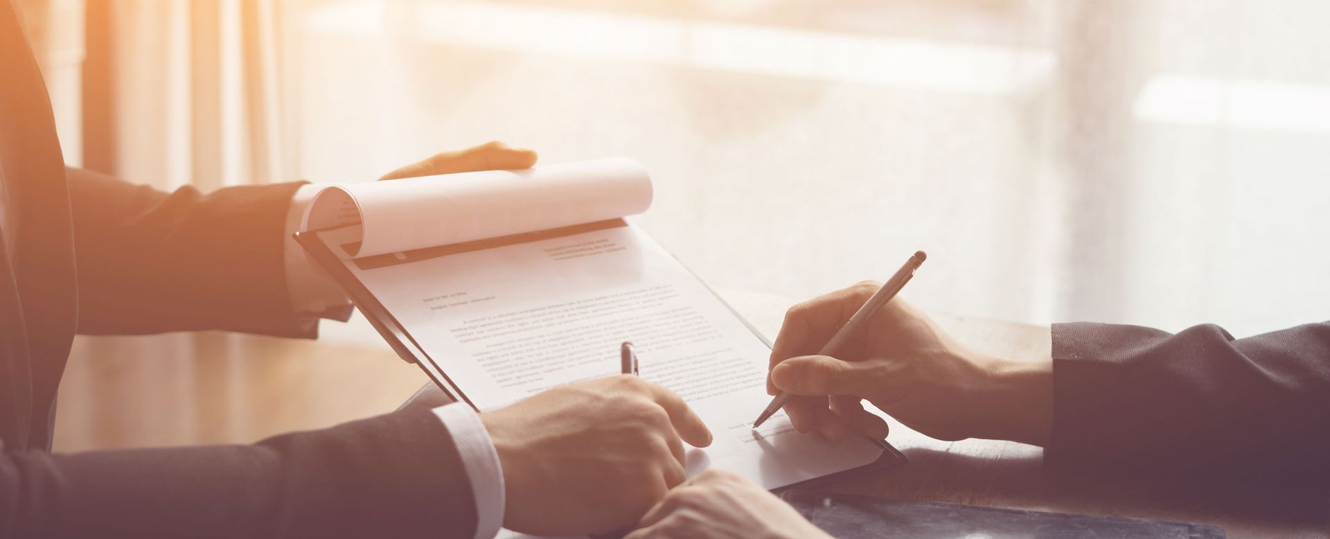 Two people signing a document at a desk in warm light
