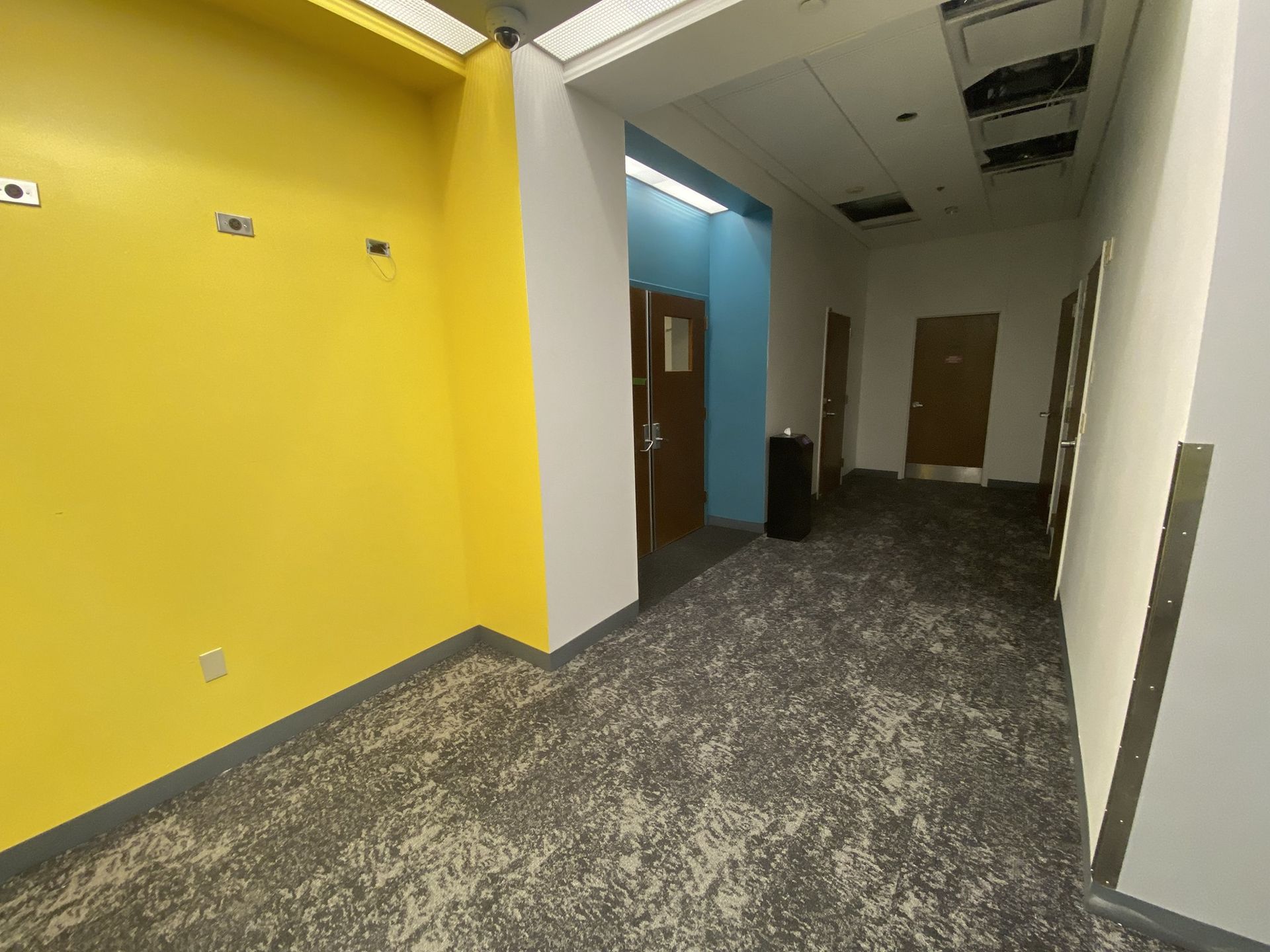 Hallway with yellow and blue walls, doors, and carpet.