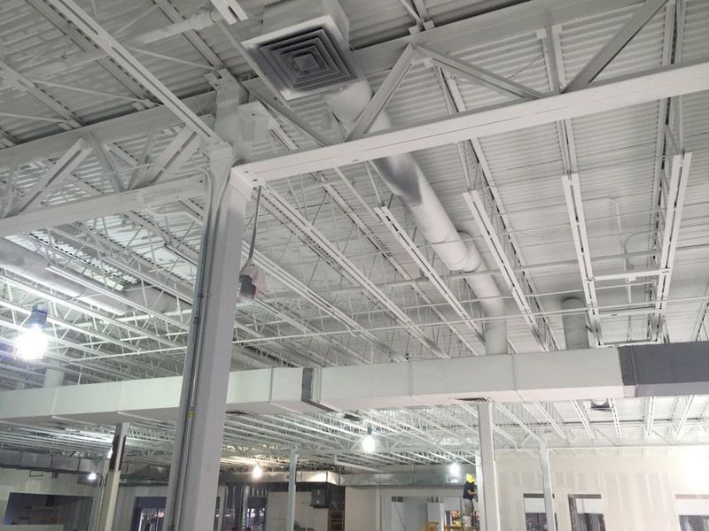 White metal ceiling with beams, ventilation, and lighting fixtures in a commercial building.