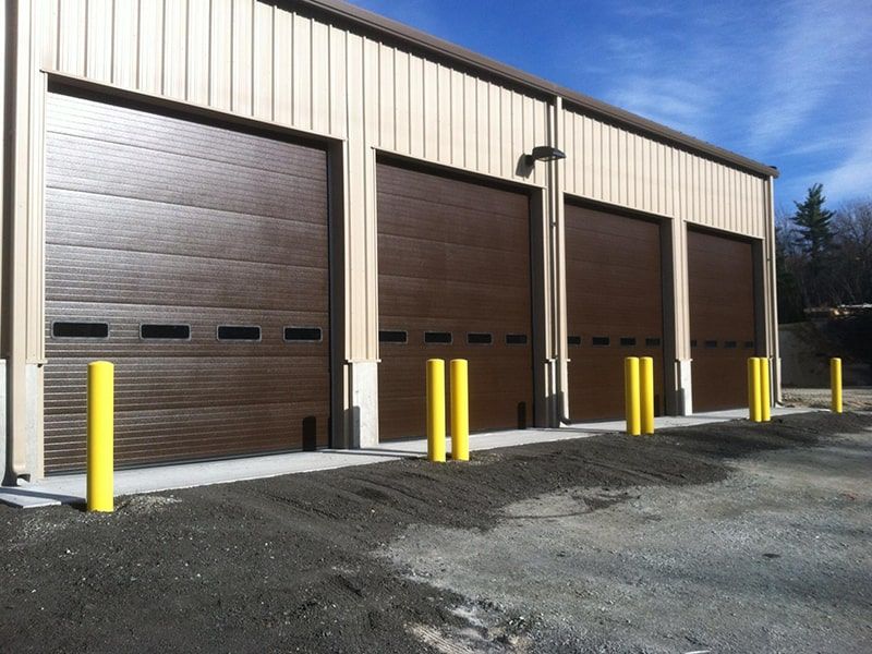 Brown garage doors on beige building with yellow safety posts.
