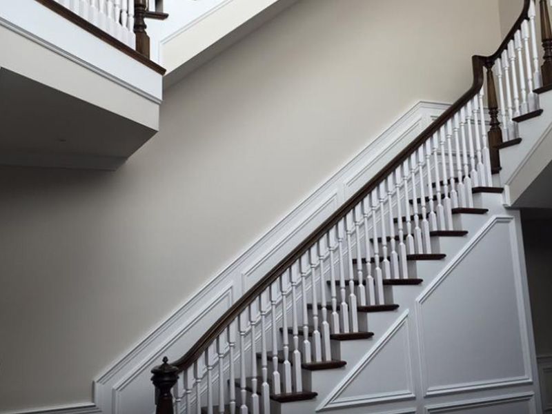 Wooden staircase with white spindles, dark wood handrail and steps, against a beige wall.