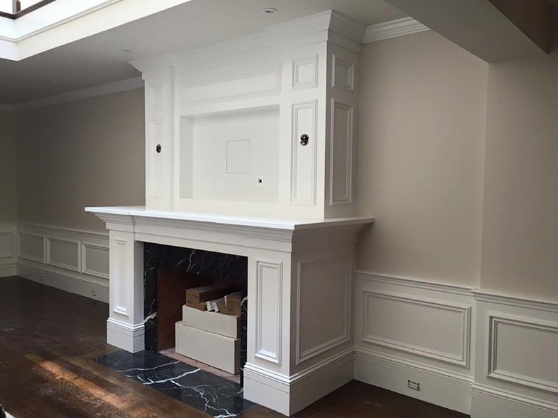 White built-in fireplace with paneling, set against neutral walls and dark flooring.