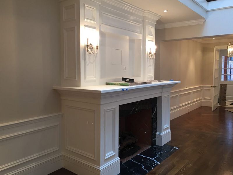 White fireplace with marble hearth and sconce lighting, set against a light-colored wall with wood flooring.