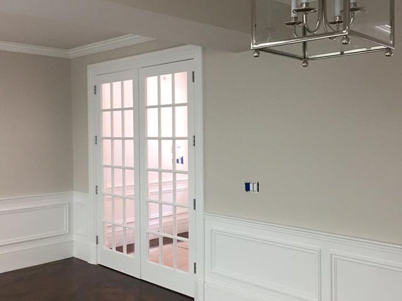 Room with French doors, white trim, beige walls, and dark hardwood floor. A chandelier hangs from the ceiling.