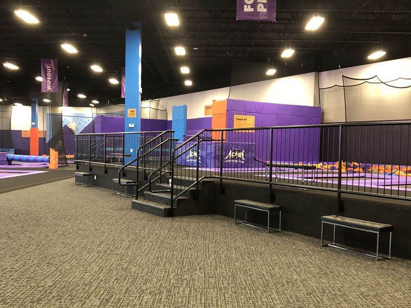 Indoor trampoline park with purple walls, black railings, and gray carpet.