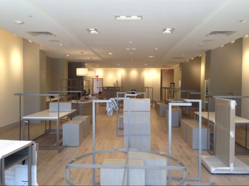 Empty retail space with gray fixtures on light wood floors and beige walls; overhead lighting.