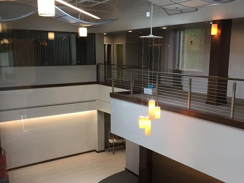 Two-story modern lobby with a balcony, glass railing, hanging lights, and white walls.