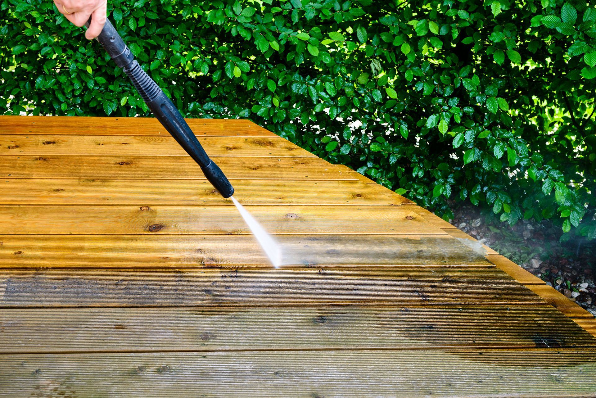 Person pressure washing a wooden deck, removing dirt.