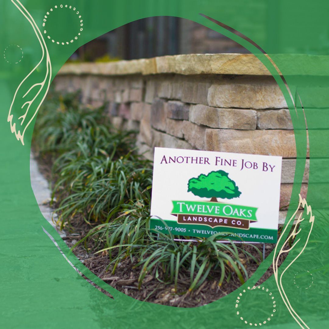 A landscaped bed of plants with a stone wall and a Twelve Oaks Landscape Co. sign.