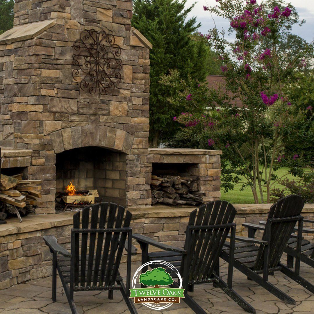 Stone fireplace with chairs, fire, and backyard setting.