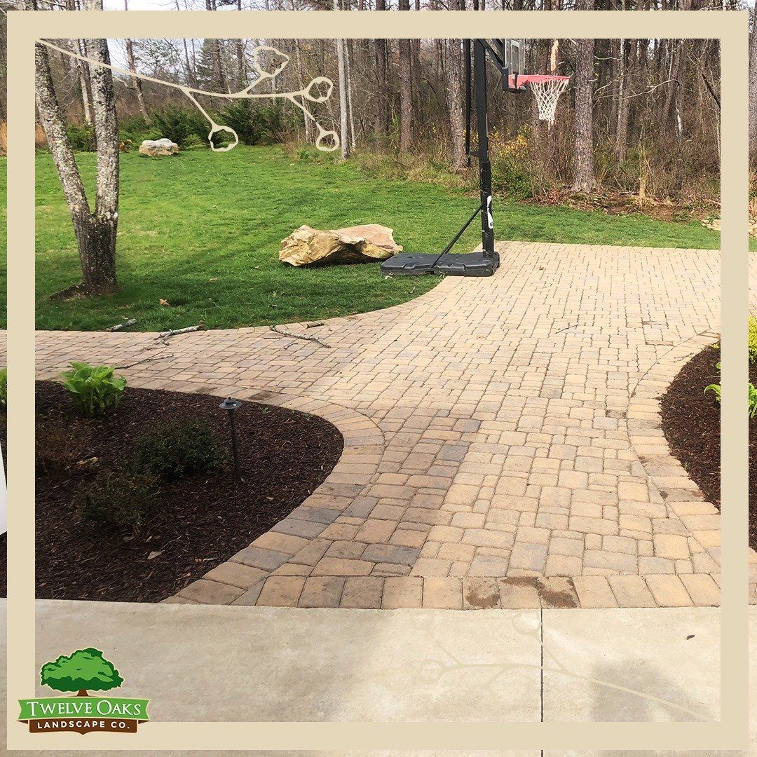 Brick pathway curves through a yard with a basketball hoop and trees.