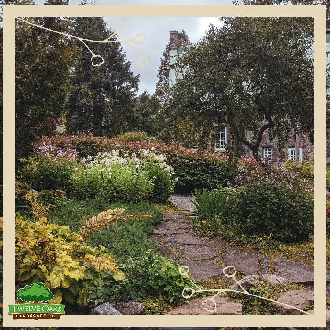 Stone path in lush garden, leading to a stone house with trees and flowers.