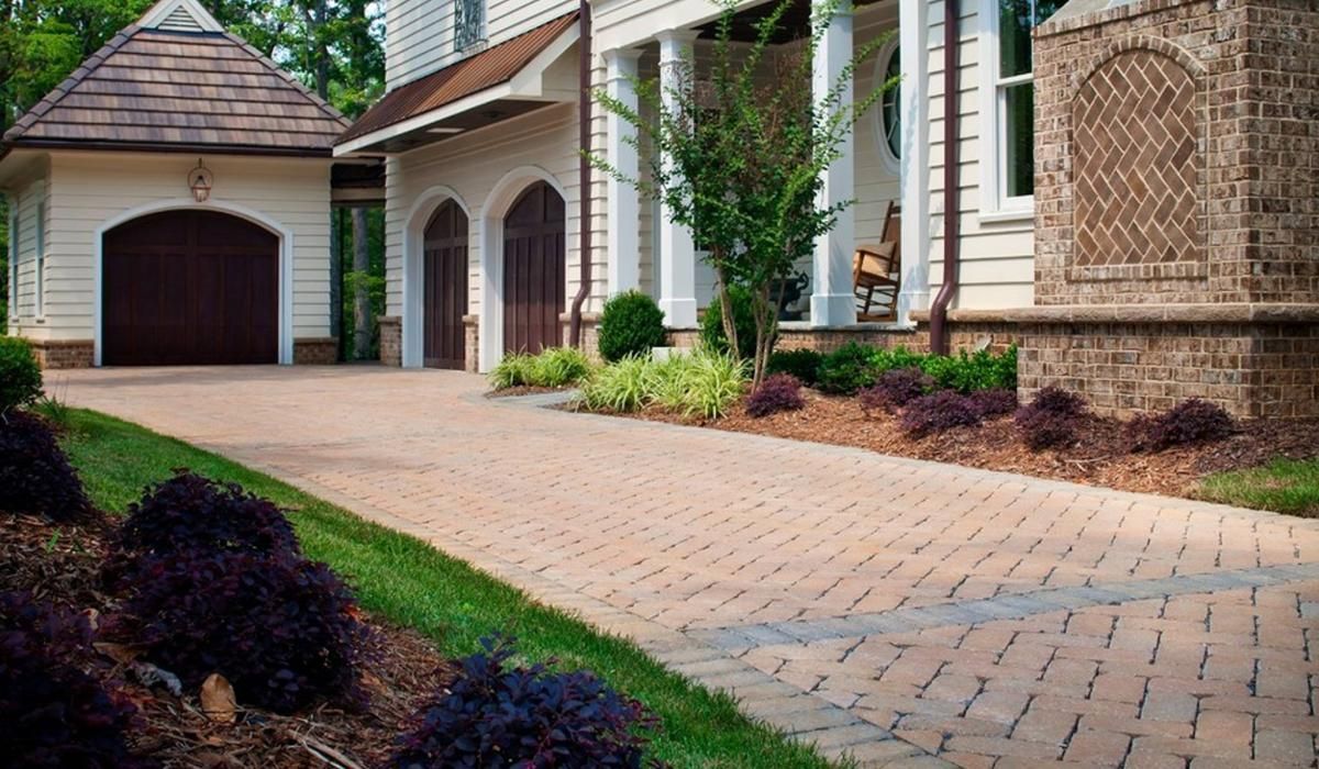 Driveway of a large house with brick and stone accents, landscaping, and a detached garage.