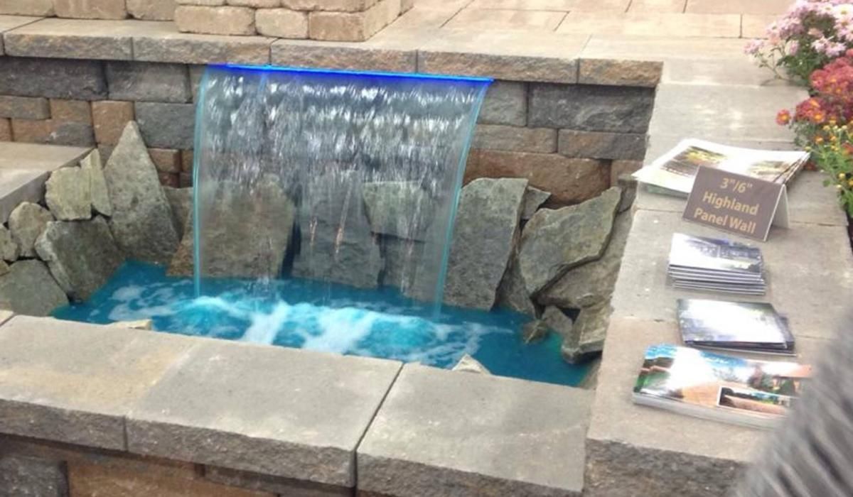 Water feature with blue-tinted water cascading over stone. Surrounded by stone bricks and rocks.