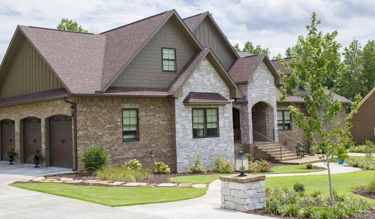 Multi-gabled brick and stone house with a three-car garage, front porch, and manicured lawn.