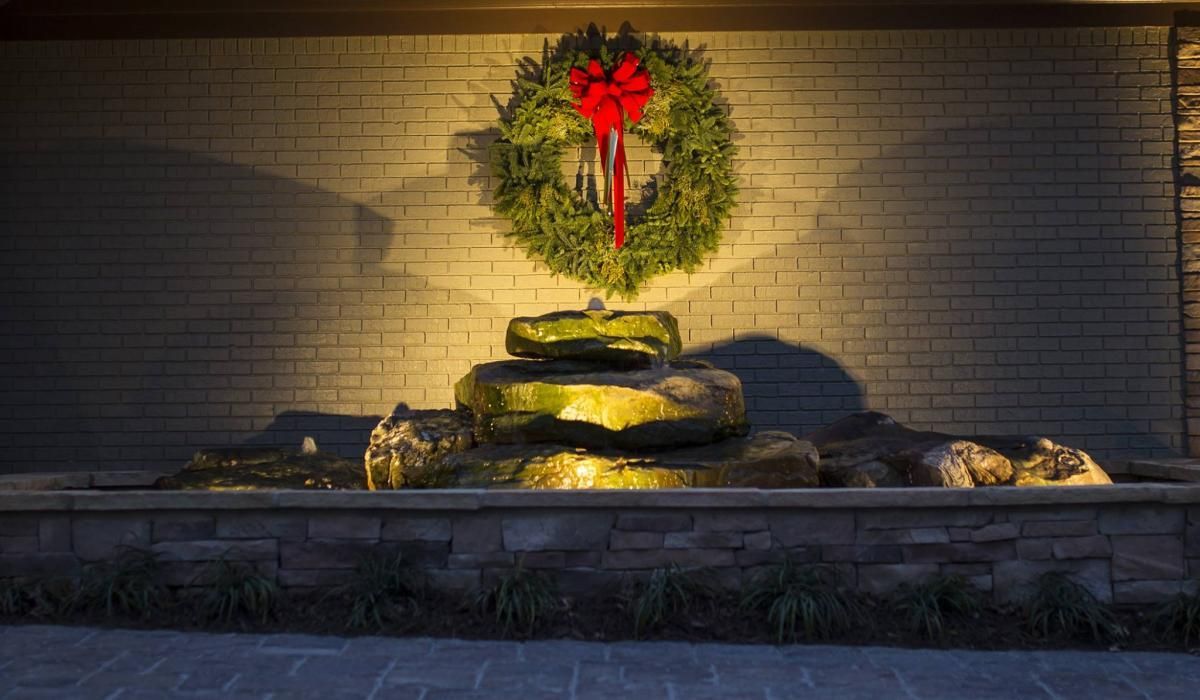 Christmas wreath with red bow above a stone fountain, lit against a brick wall.