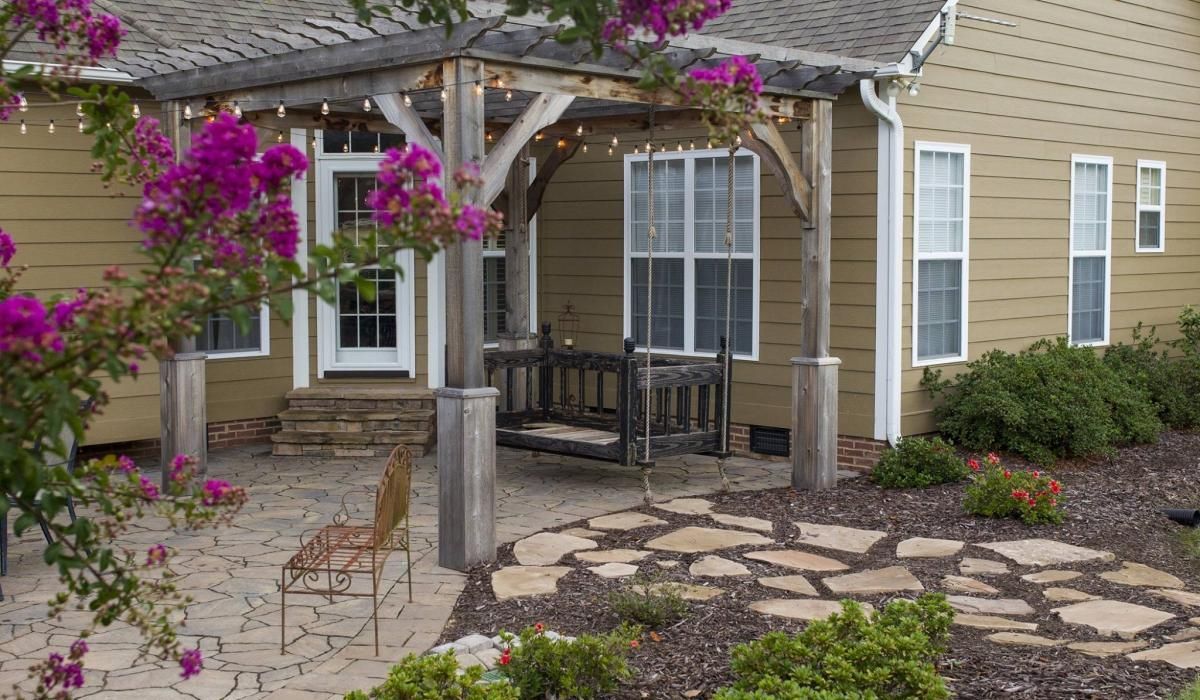 Backyard patio with a wooden pergola, swing, and colorful landscaping.