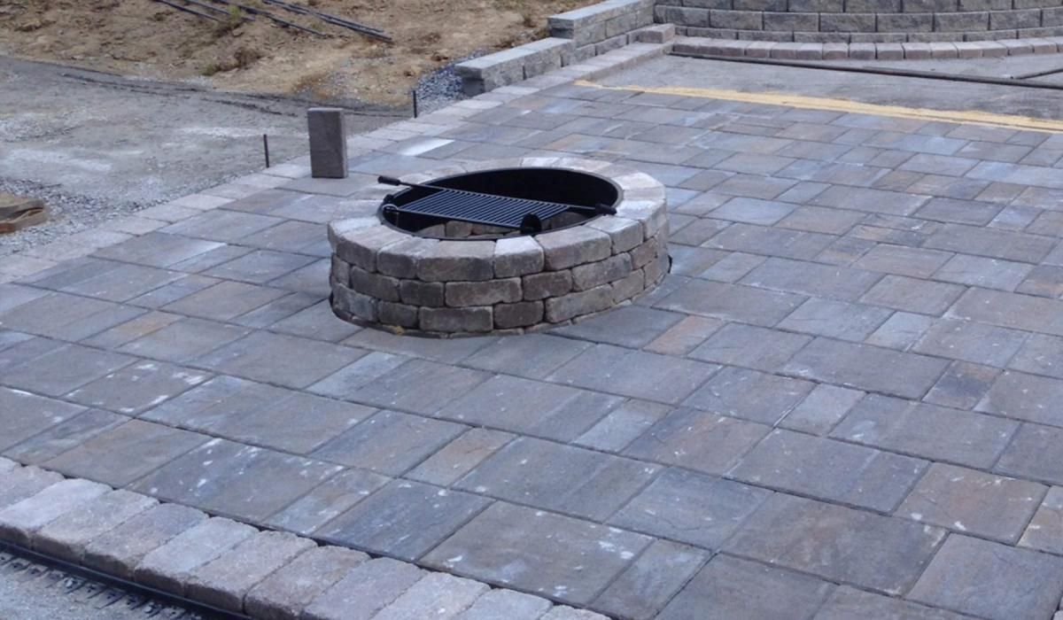 Stone patio with built-in fire pit; retaining wall in the background.