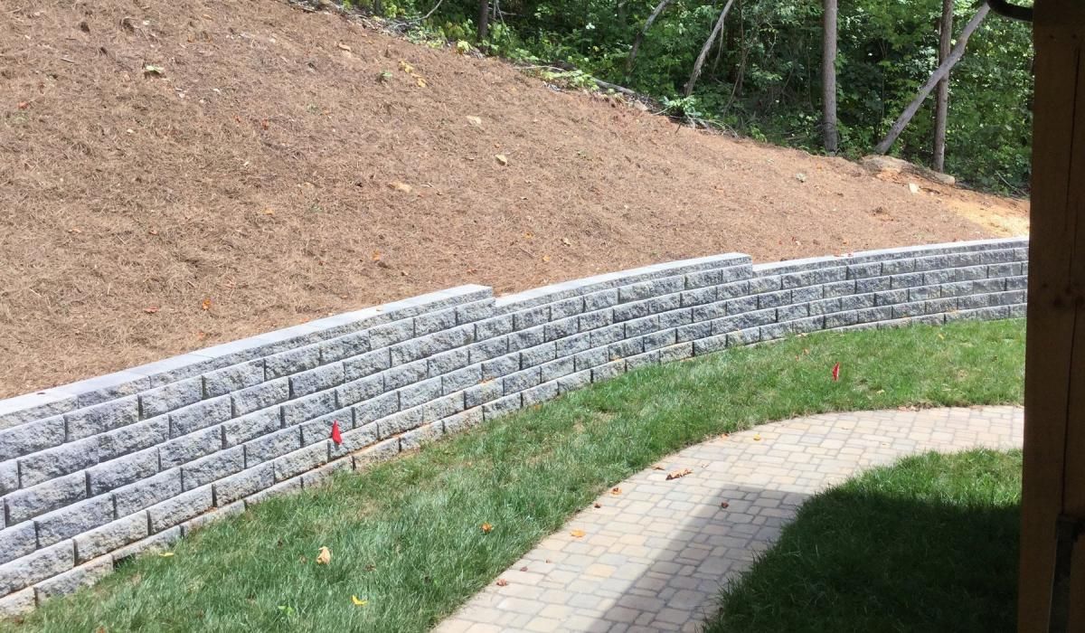 Stone retaining wall bordering a grassy area and a hillside, with a curved path.