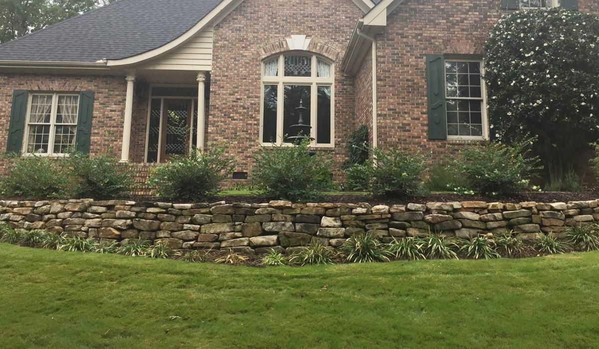 Brick house with stone retaining wall, green lawn, and shrubbery.