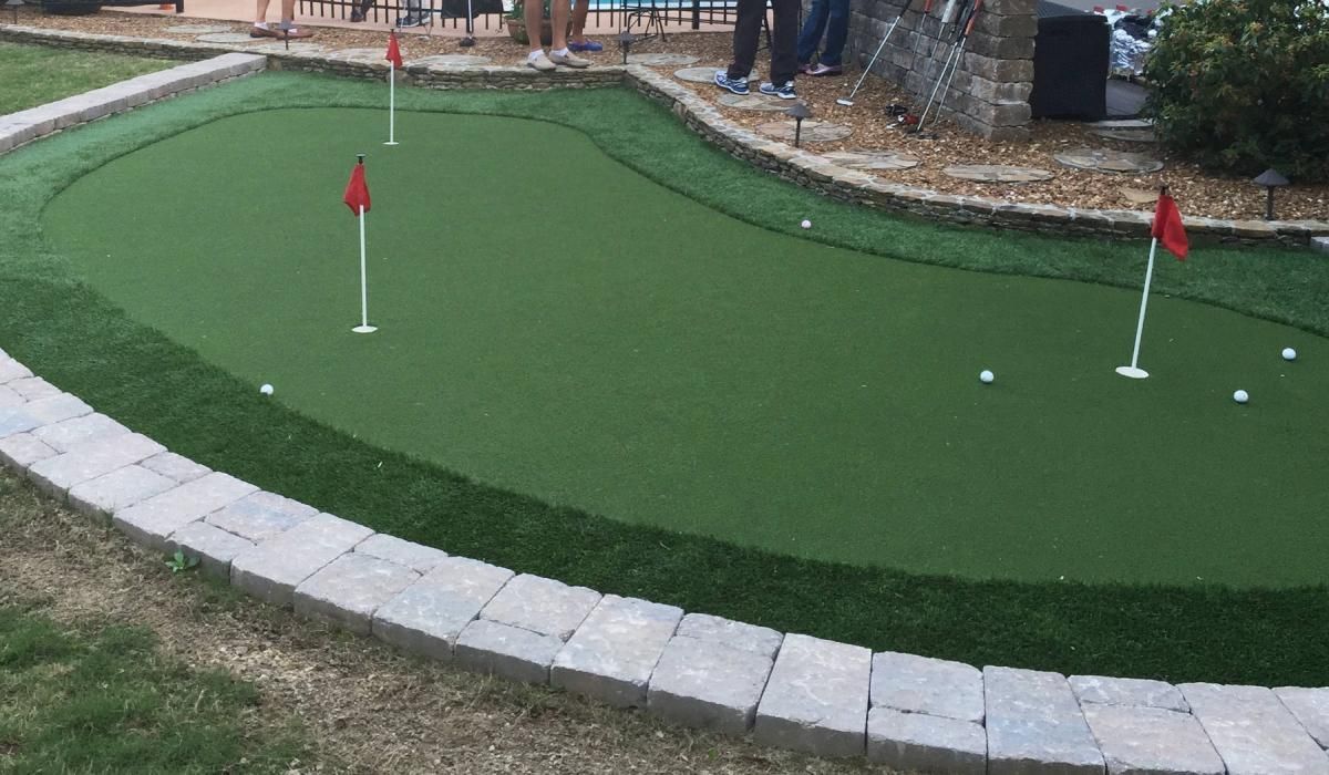 Putting green with three flags. People putting golf balls. Artificial grass with stone border.