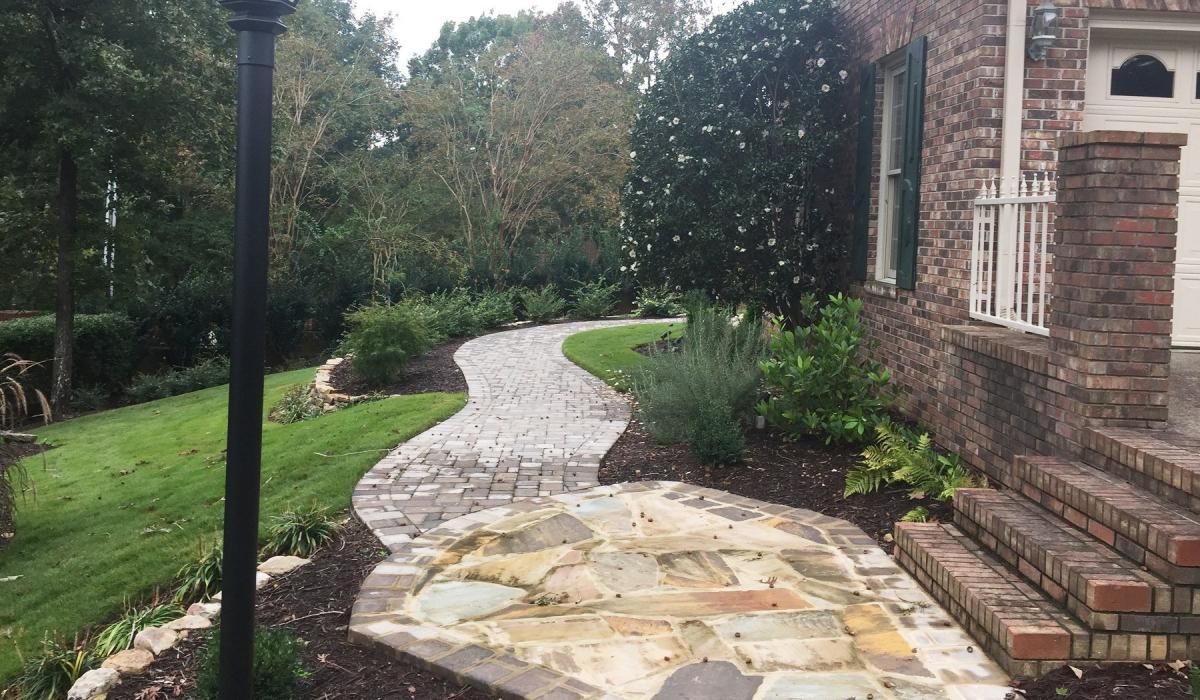 Stone path winds through landscaped yard toward a brick house with a white door.