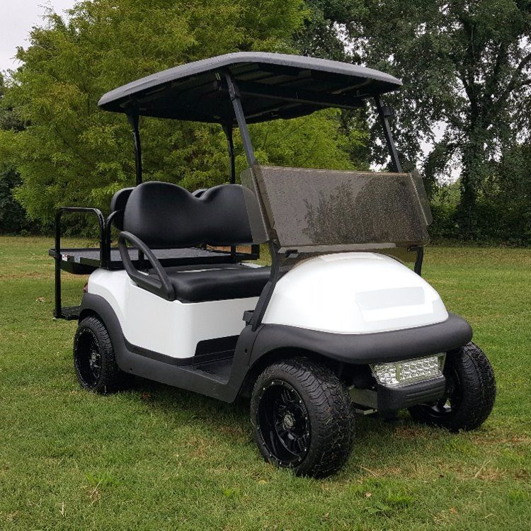 A white golf cart is parked on a lush green field.