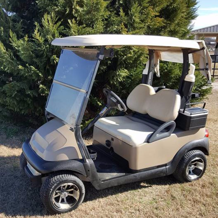 A golf cart is parked in the grass in front of trees