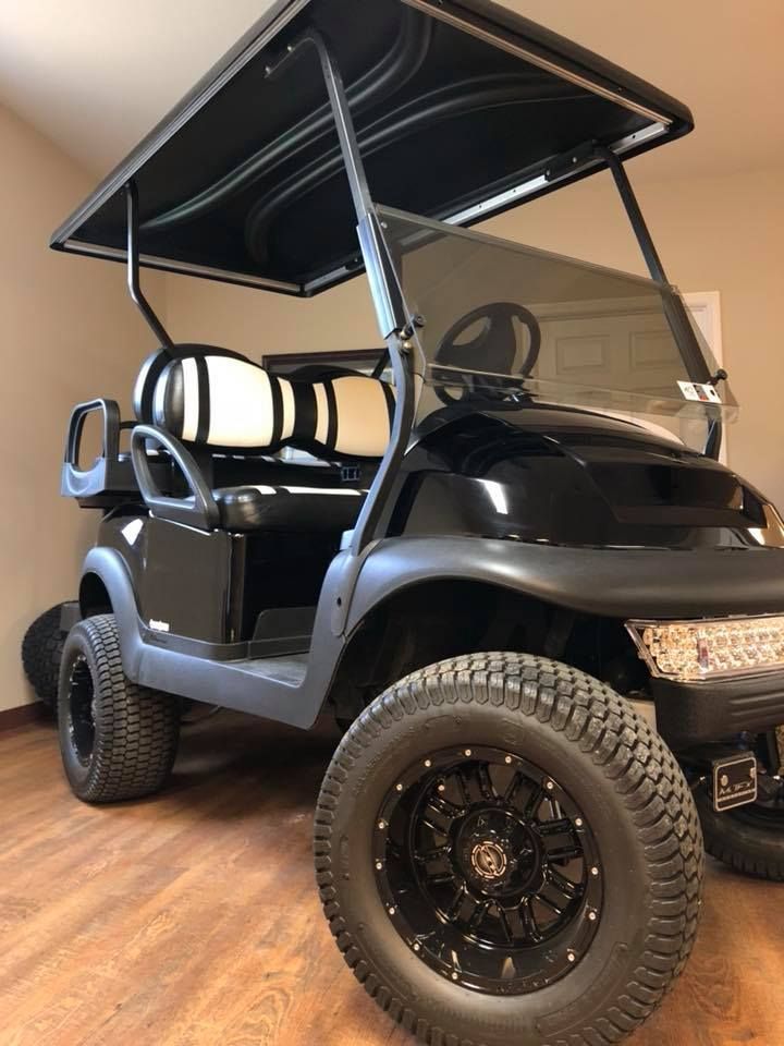 A black golf cart is parked on a wooden floor in a room.