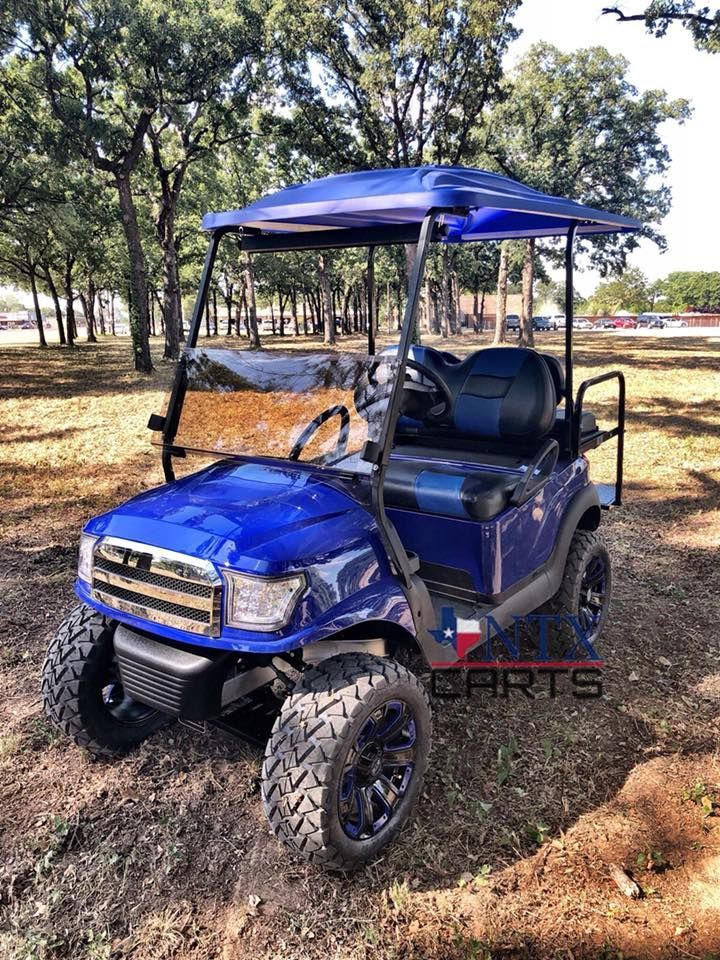 A blue golf cart is parked in the dirt in a field.