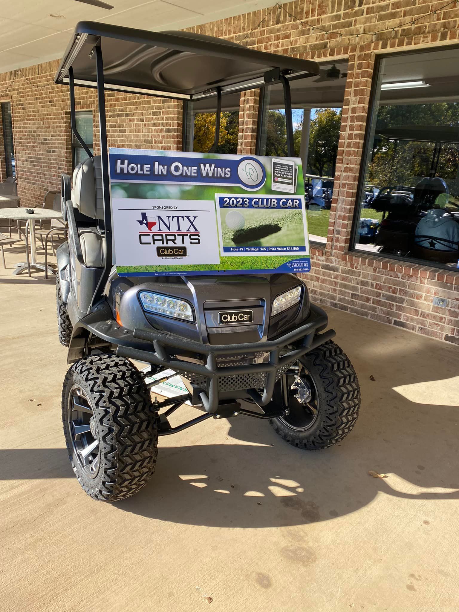 A golf cart with a sign on the front is parked in front of a brick building.