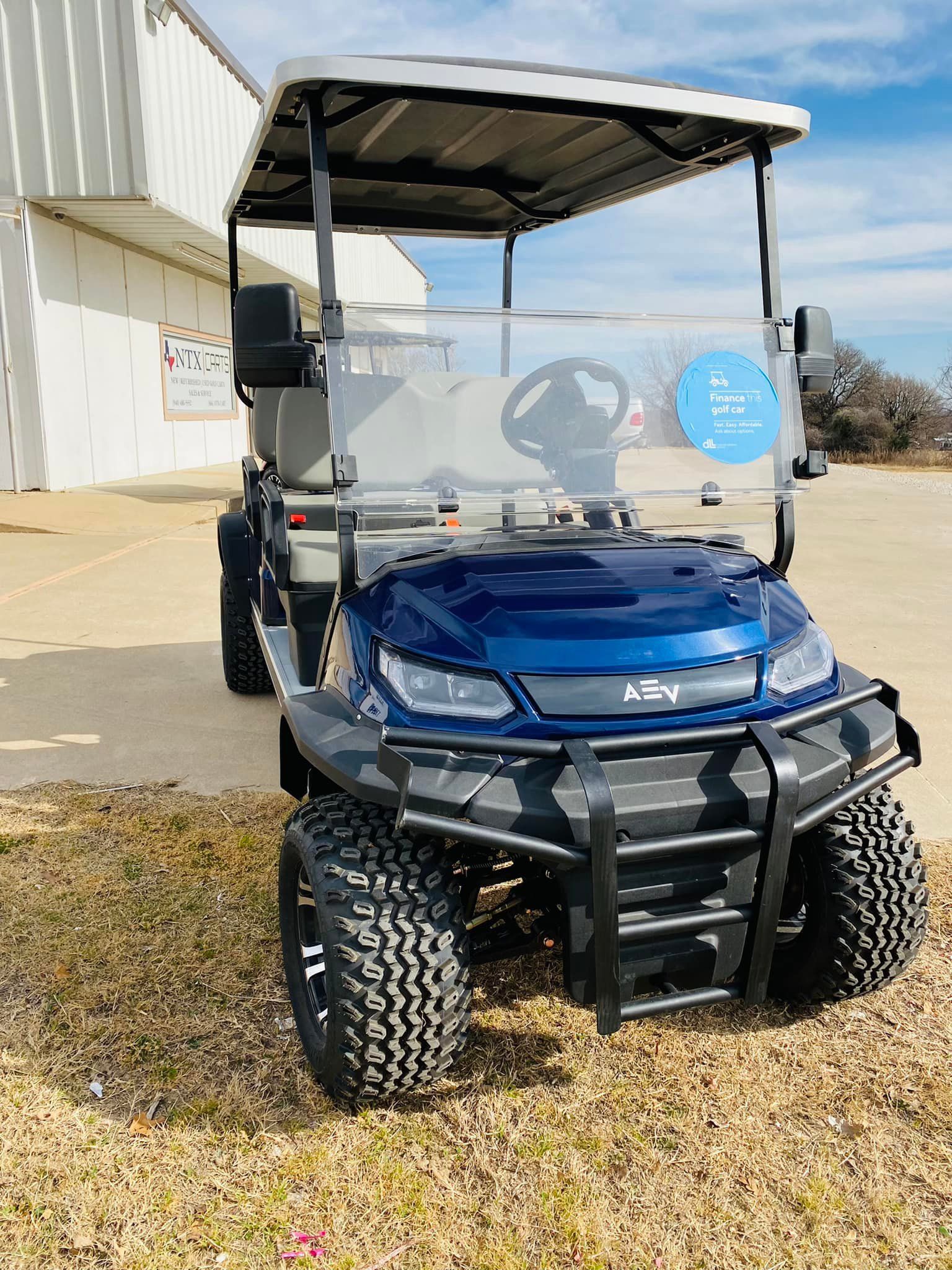 A blue golf cart is parked in a grassy area in front of a building.