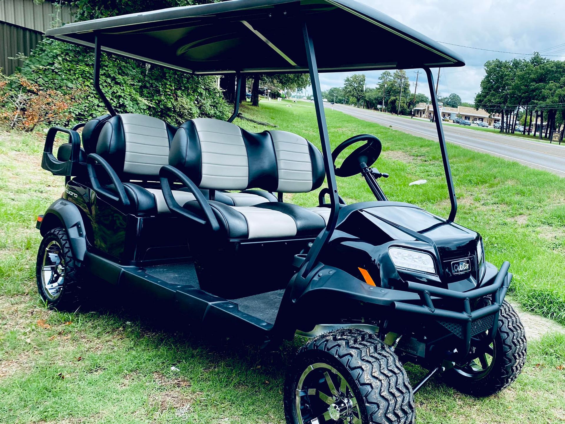 A black golf cart with a canopy is parked in a grassy field.